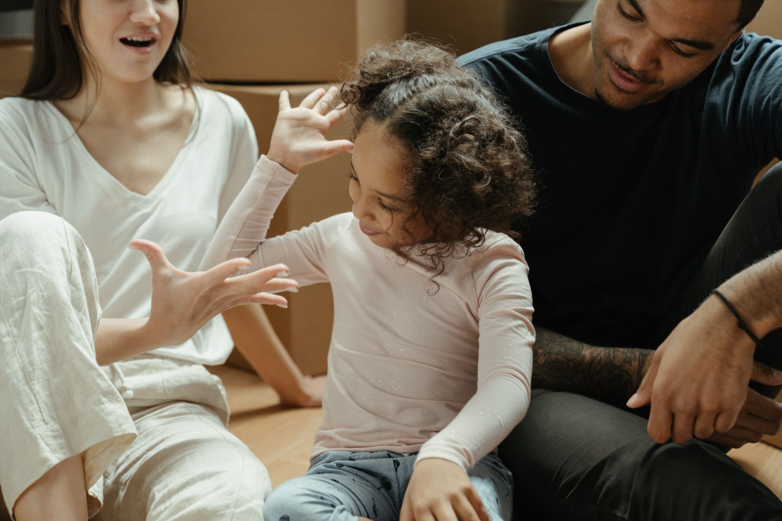 Mergaitė sėdi ant grindų tarp savo tėvų, ji tiesia ranką mamai, o mama - mergaitei, pexels.com nuotr.