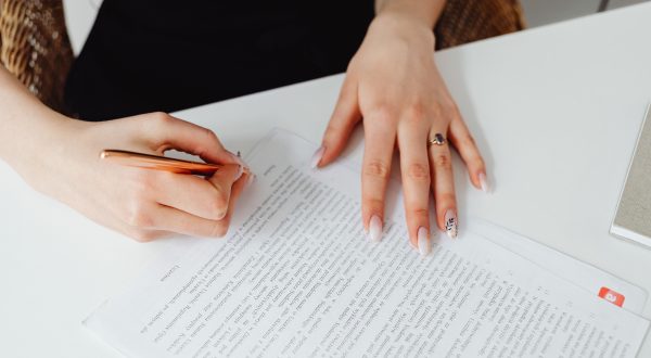 Moteris rašikliu pasirašo ant stalo padėtą dokumentą, pexels.com nuotr.