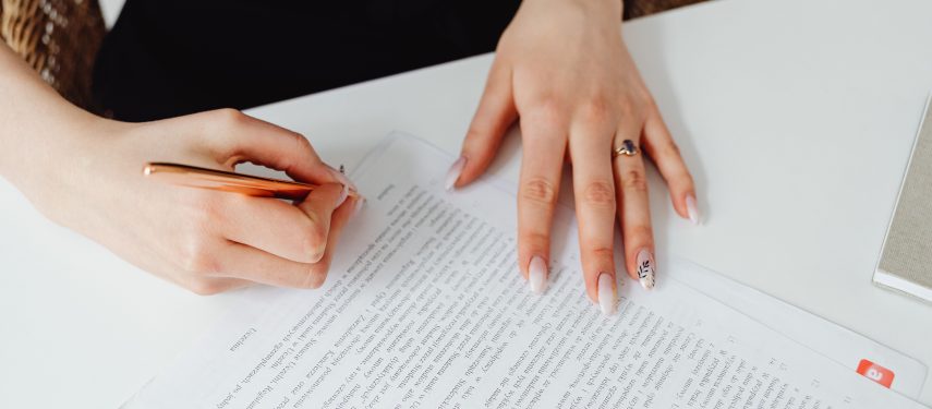 Moteris rašikliu pasirašo ant stalo padėtą dokumentą, pexels.com nuotr.