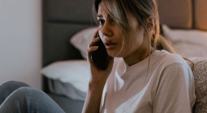 Susirūpinusi moteris sėdi prie lovos ir kalba mobiliuoju telefonu, pexels.com nuotr.