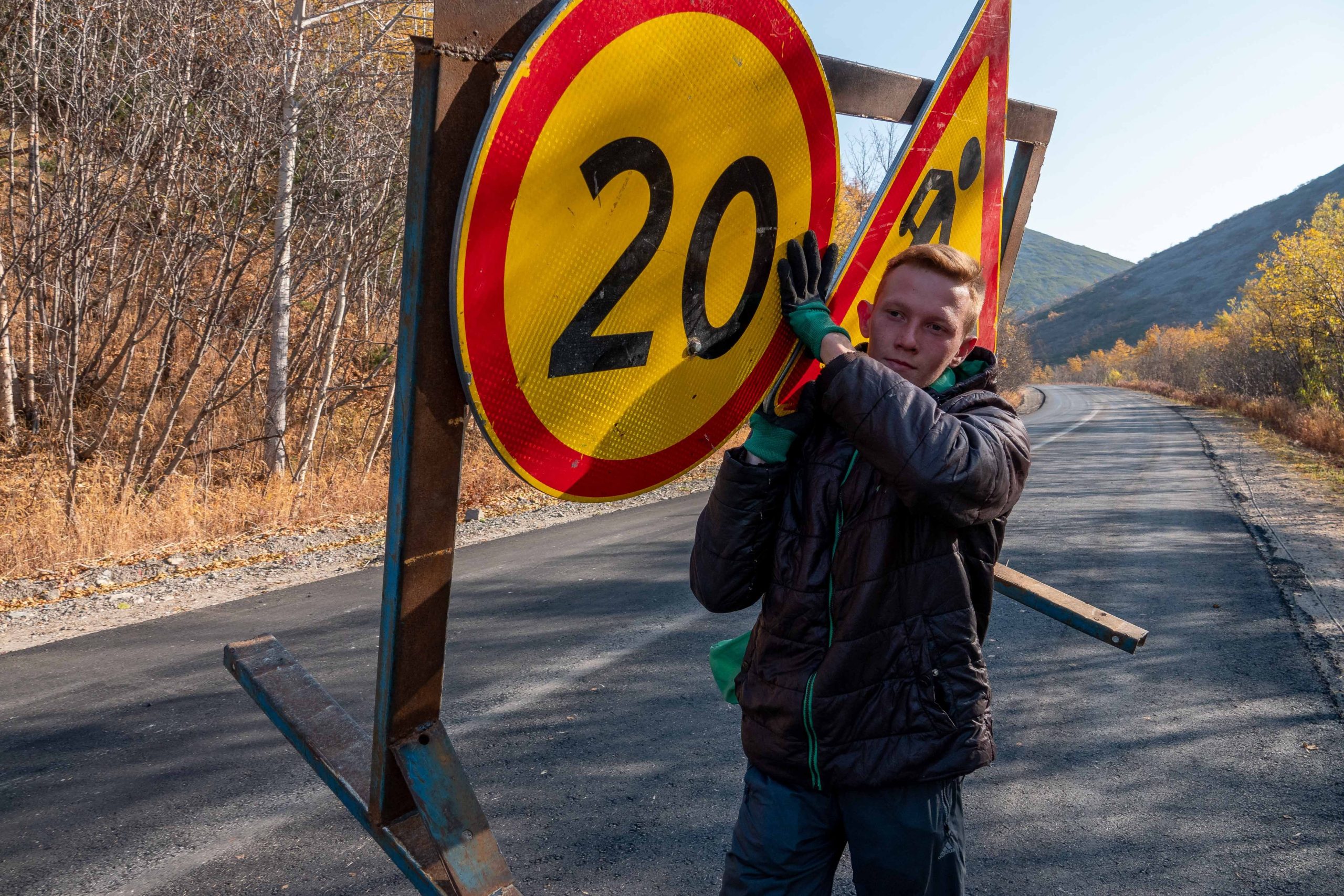 Kelio tvarkymo darbuotojas laiko 20 km/val. greičio ribojimo ir kelio darbų ženklus, pexels.com nuotr.