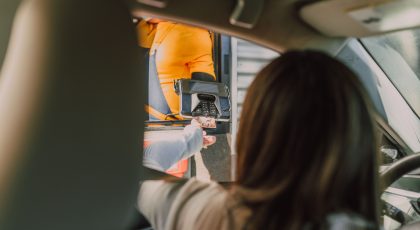 Moteris sėdi mašinoje, ji apmoką užsakymą kortelių skaičiuotuve, kurį laiko darbuotojas iškišęs ranką per langelį, pexels.com nuotr.
