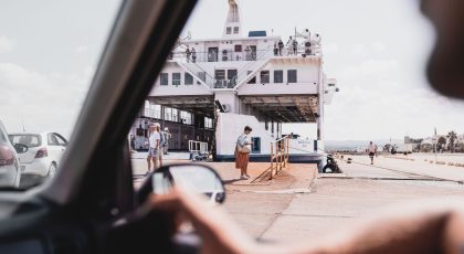 Iš automobilio vidaus matomas prieplaukoje stovintis keltas, į kurį įvažiuoja transporto priemonės, stovi žmonės, pexels.com nuotr.