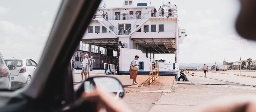 Iš automobilio vidaus matomas prieplaukoje stovintis keltas, į kurį įvažiuoja transporto priemonės, stovi žmonės, pexels.com nuotr.